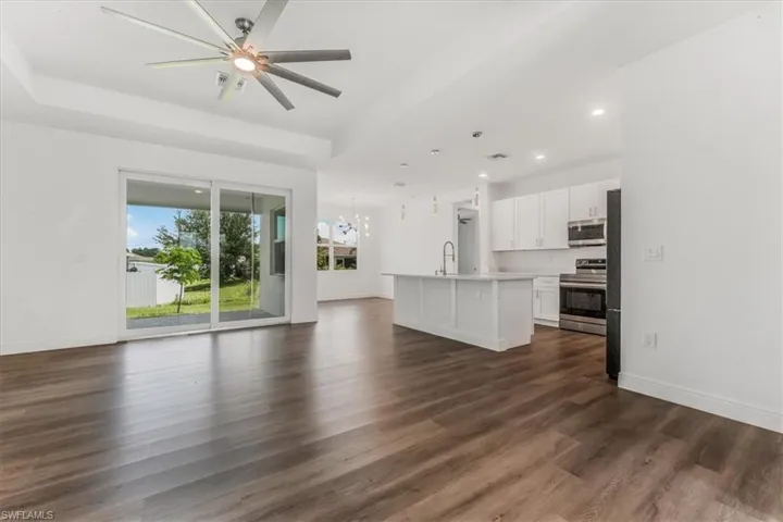 Unfurnished living room featuring dark wood finished floors, a raised ceiling, ceiling fan, recessed lighting, and a chandelier