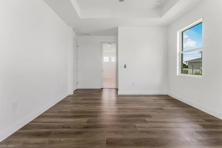Unfurnished room featuring a tray ceiling and dark wood-style flooring
