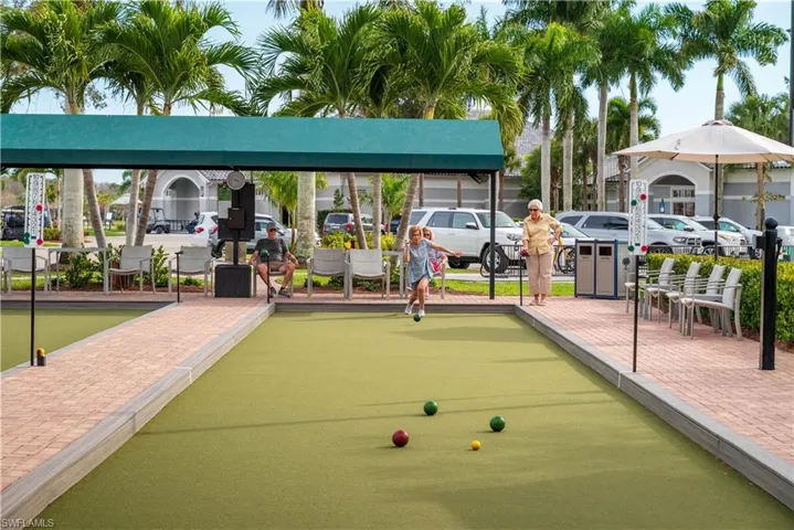 Bocce ball court featuring a green playing surface, brick paver walkways, a shaded seating area, and palm tree landscaping