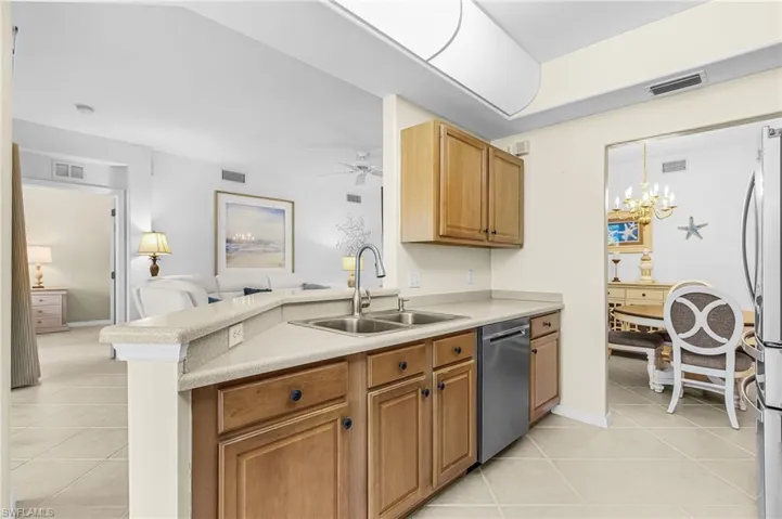 Kitchen featuring wood cabinetry, stainless steel dishwasher, double basin sink with gooseneck faucet, and light-toned countertops