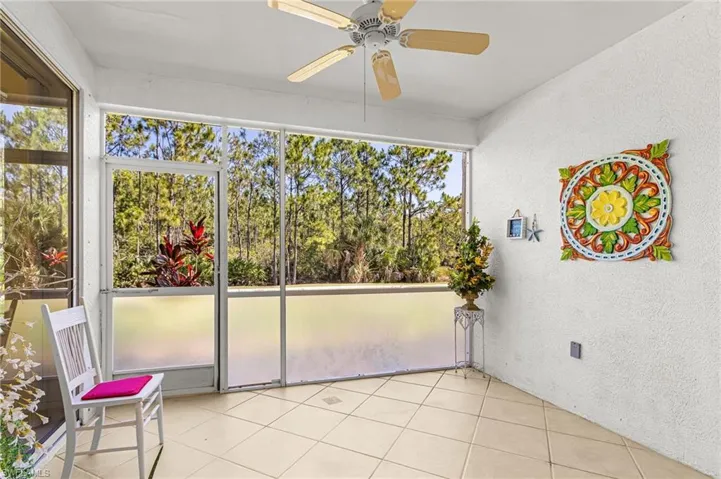 Screened-in patio featuring ceramic tile flooring, a ceiling fan, and a serene treeline backdrop