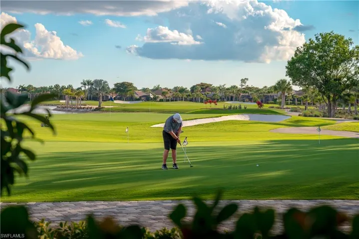 Expansive golf course green featuring a sand trap, water feature, and mature palm trees
