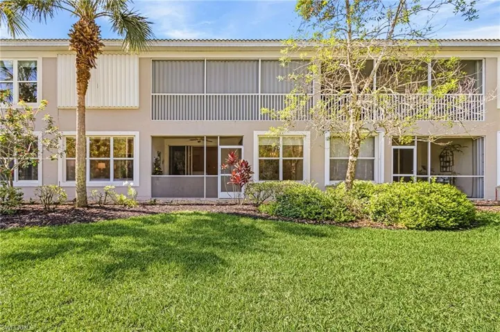 Exterior facade featuring multiple screened balconies and patios, mature landscaping, and a manicured lawn
