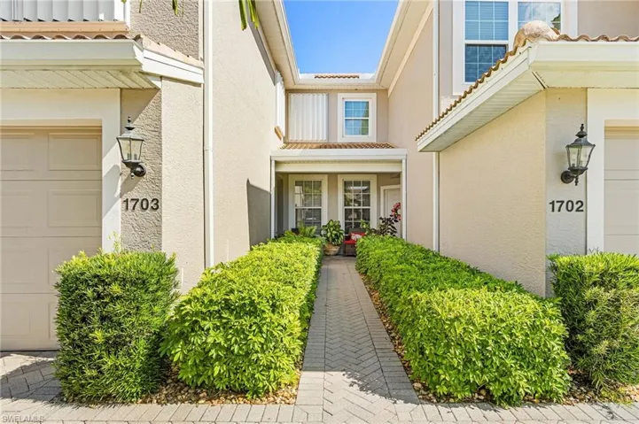 Paver walkway bordered by manicured hedges leading to a covered entryway