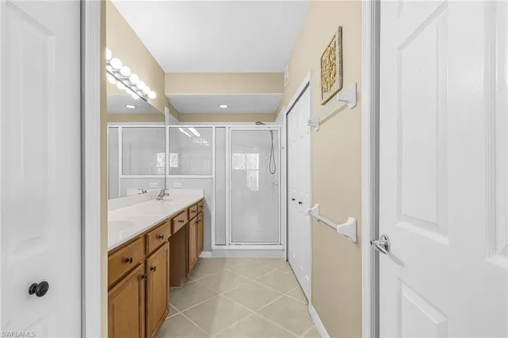 Bathroom featuring a double vanity with light wood cabinetry and white countertops, a large mirror, and a glass-enclosed shower