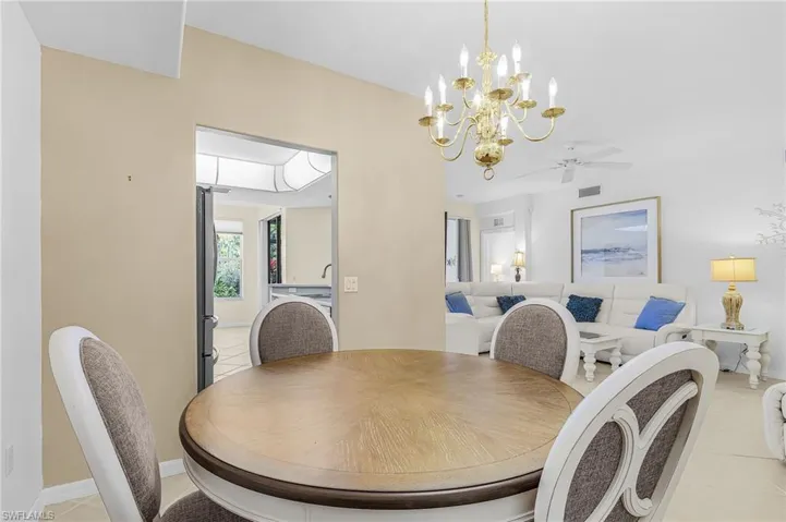 Dining area featuring a brass chandelier, wood-finish flooring, and a cased opening to a bright kitchen with a skylight