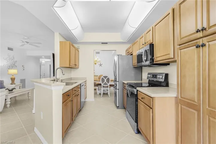 Kitchen featuring wood cabinetry, stone countertops, stainless steel appliances, tile flooring, and integrated ceiling lighting