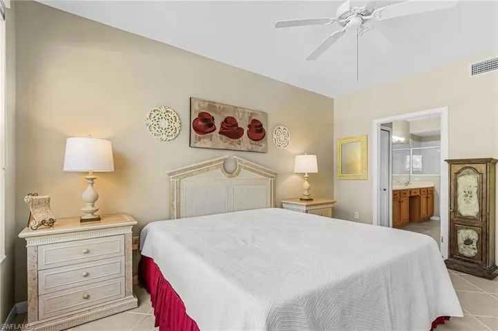 Neutral tone bedroom featuring a ceiling fan, tiled flooring, and a cased opening revealing a bathroom with a wood-finish vanity