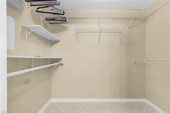 Walk-in closet with beige walls, white wire shelving, a white hanging rod, and light-colored tile flooring