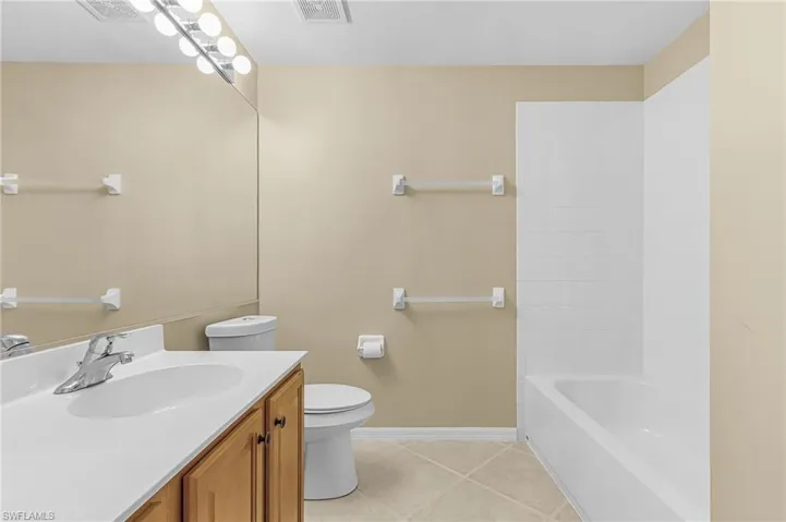 Bathroom featuring a wood-finish vanity with a white countertop and integrated sink, a large mirror, a chrome faucet, and a shower-tub combination with white subway tile surround