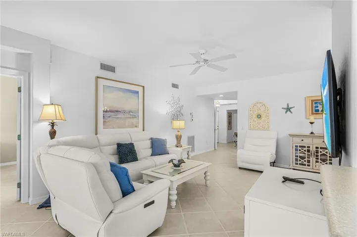 Spacious living area featuring neutral tile flooring, white walls, and a ceiling fan