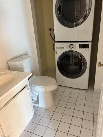 Half bathroom with vanity, light tile patterned flooring, and stacked washer / dryer