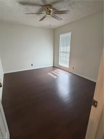 Unfurnished room with ceiling fan, a textured ceiling, and dark wood-style floors