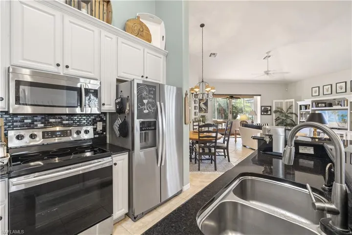 Kitchen with decorative backsplash, appliances with stainless steel finishes, ceiling fan with notable chandelier, sink, and white cabinets