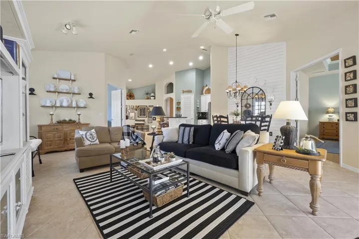 Living room with ceiling fan with notable chandelier, light tile patterned floors, and high vaulted ceiling