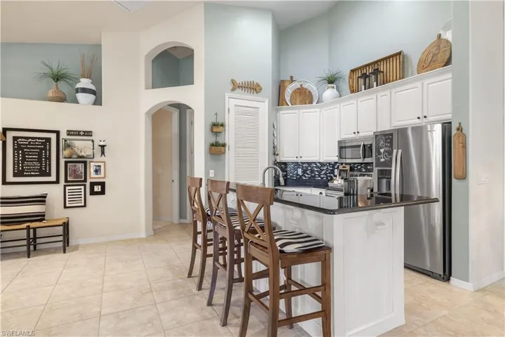 Kitchen with a kitchen bar, a towering ceiling, stainless steel appliances, a center island with sink, and white cabinets