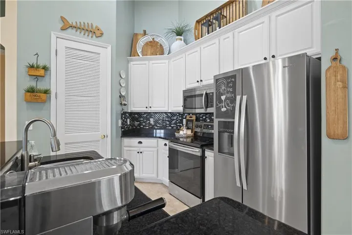 Kitchen with tasteful backsplash, white cabinetry, light tile patterned floors, and appliances with stainless steel finishes
