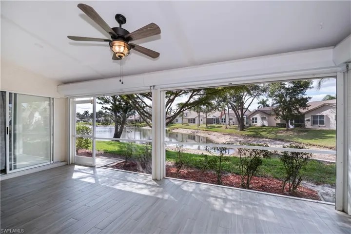Unfurnished sunroom featuring a ceiling fan, a water view, a residential view, and a healthy amount of sunlight