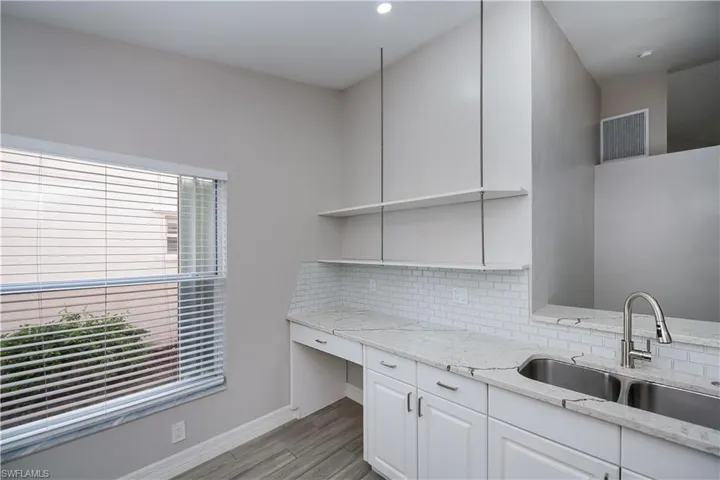 Kitchen featuring visible vents, decorative backsplash, white cabinets, light stone counters, and a sink