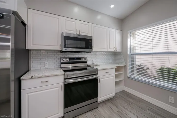 Kitchen with open shelves, appliances with stainless steel finishes, white cabinetry, and tasteful backsplash
