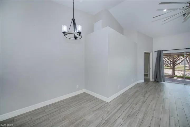 Unfurnished room with ceiling fan with notable chandelier, light wood finished floors, and baseboards