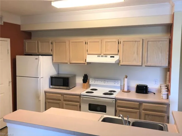Kitchen with white appliances, crown molding, under cabinet range hood, and light countertops