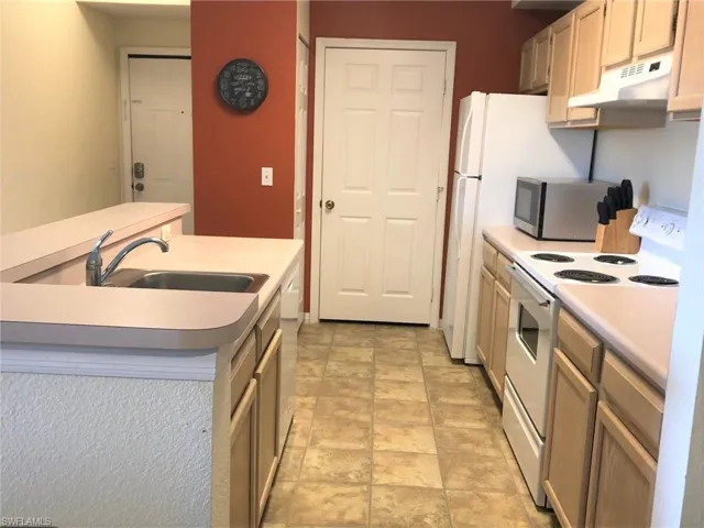 Kitchen with light countertops, stainless steel microwave, under cabinet range hood, white range with electric cooktop, and a sink