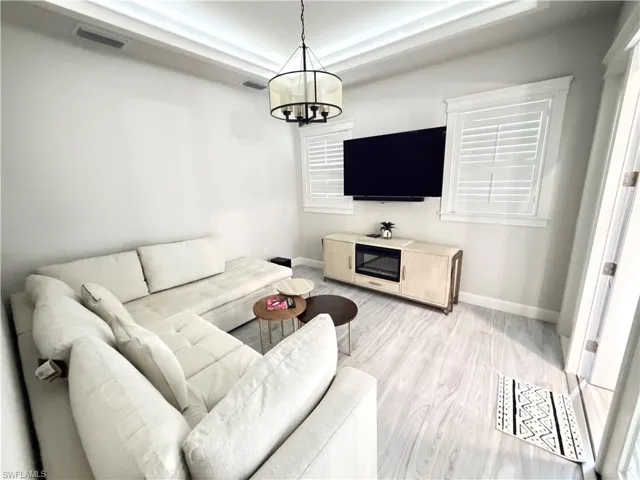 Living area with light wood-style floors, a tray ceiling, and a chandelier