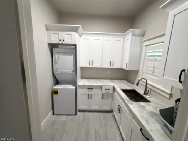Laundry room with stacked washer / drying machine, cabinet space, and light wood finished floors