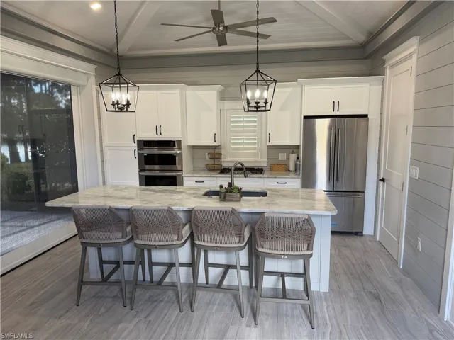 Kitchen with hanging lights, stainless steel appliances, a breakfast bar area, light stone countertops, and a center island with sink