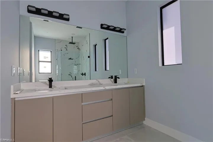 Dual vanity featuring matte black faucets, a full-width mirror, and two contemporary light fixtures