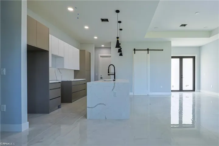 Kitchen featuring a barn door, modern cabinets, white cabinetry, light stone countertops, and decorative light fixtures