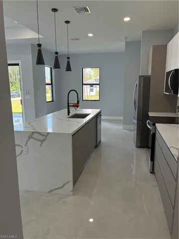 Kitchen featuring a waterfall-edge island with a built-in sink and matte black faucet, modern pendant lighting, recessed lighting, stainless steel appliances, and large format tile flooring