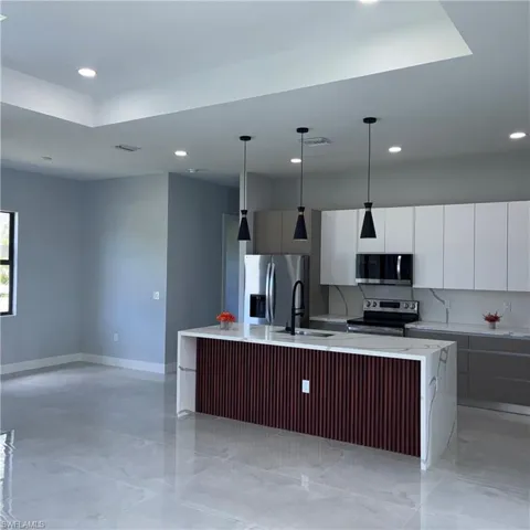 Modern kitchen featuring a waterfall island with fluted wood-finish paneling, under-mount sink, and three pendant lights