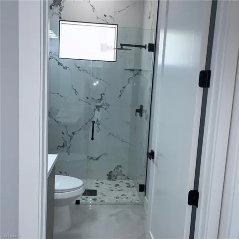 Contemporary shower enclosure featuring clear glass panels, matte black hardware, and large format marble-look wall tiles