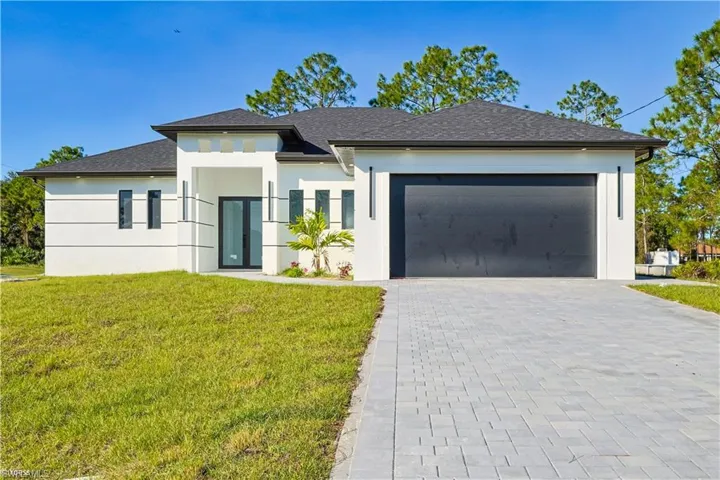 Prairie-style home featuring a front yard, decorative driveway, stucco siding, roof with shingles, and an attached garage