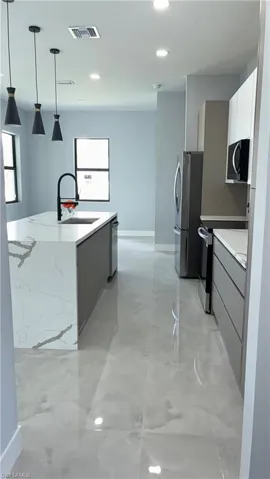 Kitchen featuring an oversized island with a waterfall countertop and undermount sink, modern pendant lighting, stainless steel appliances, and sleek flat-panel cabinetry