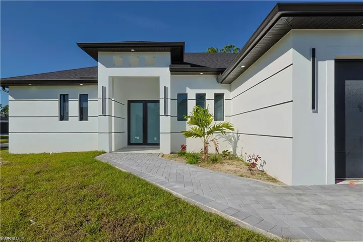 View of exterior entry with stucco siding, a shingled roof, and a yard