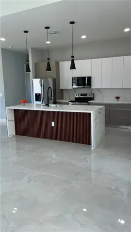 Spacious kitchen featuring a large waterfall-edge island with wood-slat detailing, complemented by three pendant lights