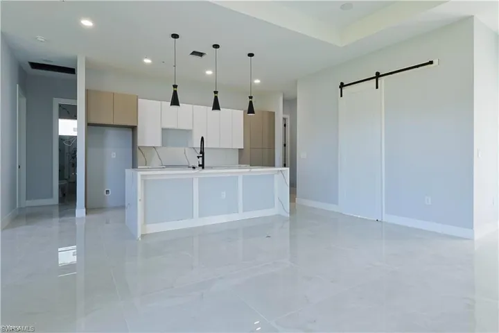 Kitchen featuring a barn door, modern cabinets, an island with sink, decorative light fixtures, and recessed lighting