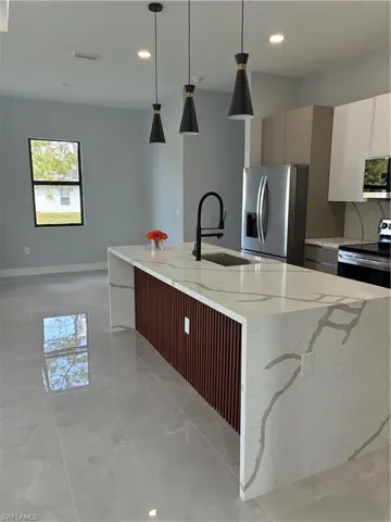 Kitchen island featuring a waterfall countertop with veining, three pendant lights, a built-in sink with a matte black faucet, wood-look paneling, and ceramic tile flooring