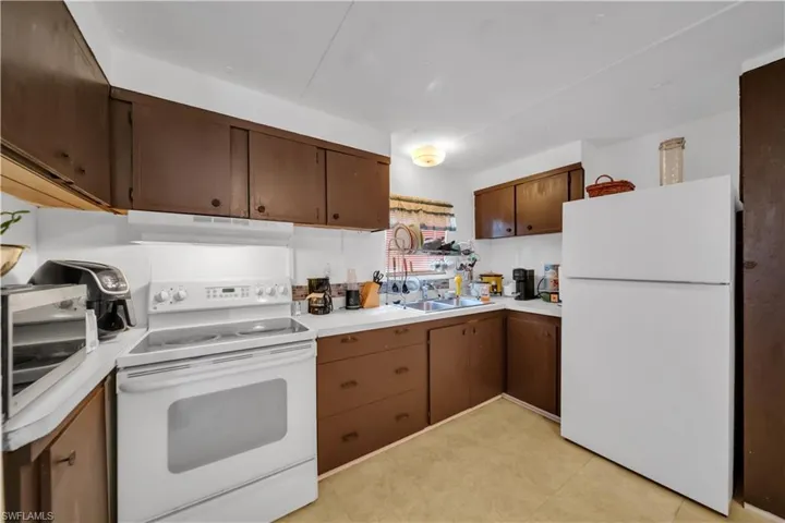 Kitchen with white appliances, under cabinet range hood, a sink, and light countertops