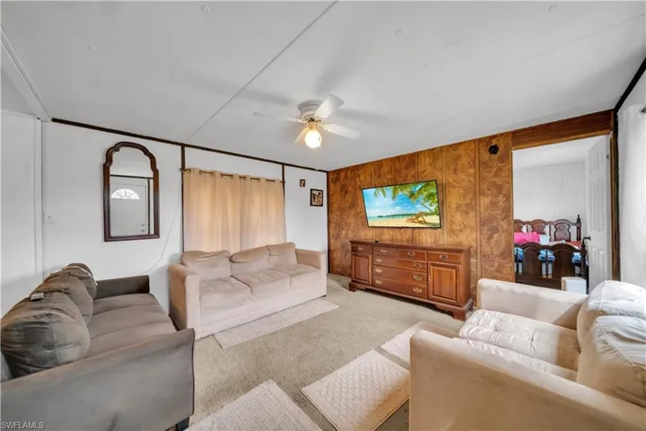 Living area with light colored carpet, ceiling fan, and wooden walls