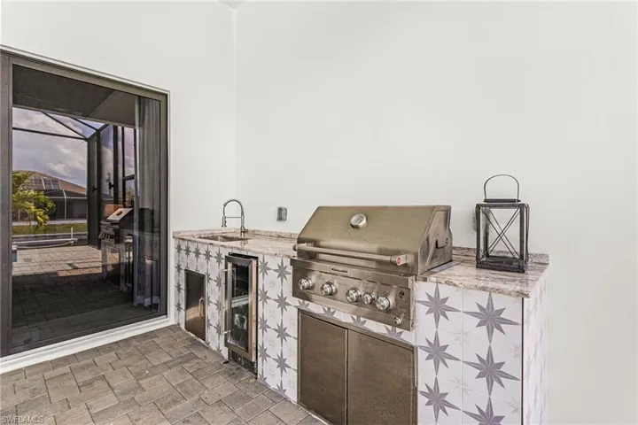 Outdoor kitchen featuring an integrated stainless steel grill, beverage refrigerator, and sink