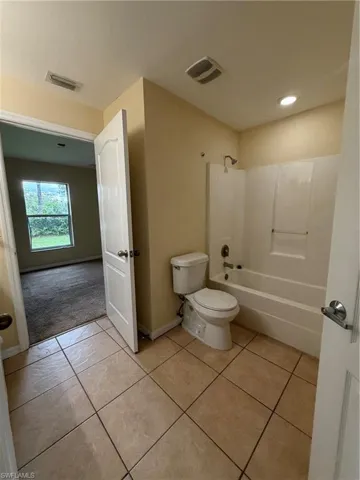 Tiled flooring with a white tub/shower combination, toilet, and recessed lighting