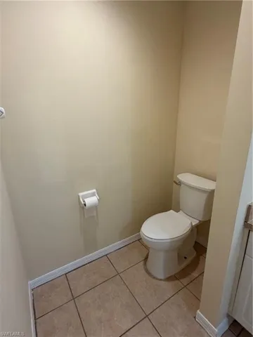 Neutral-toned ceramic tile flooring, a standard toilet, and light-colored walls