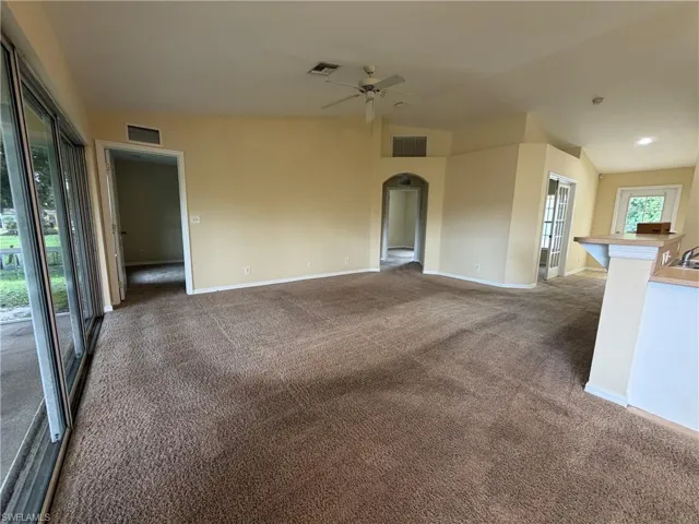 Expansive carpeted area featuring a ceiling fan, sliding glass doors, arched doorway, and a breakfast bar with light wood-finish countertop