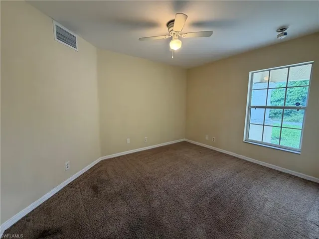 Carpeted flooring, ceiling fan with integrated lighting, wall-mounted light fixture, window with exterior landscape, and a wall-mounted vent
