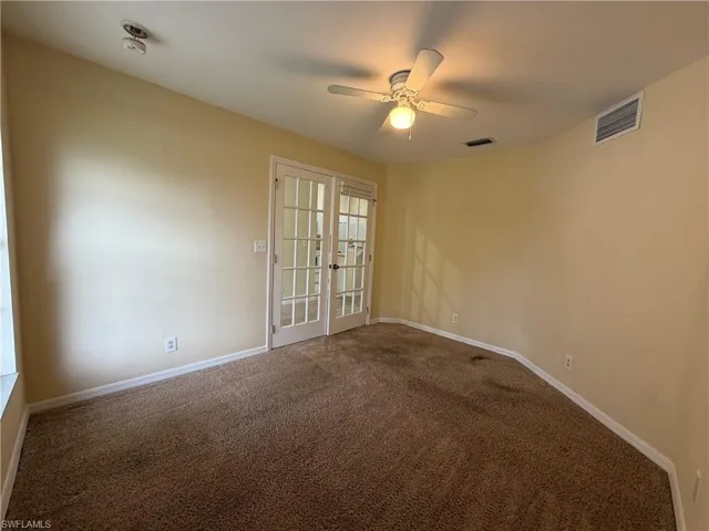 Carpeted room featuring a ceiling fan with integrated lighting and double French doors with glass panes