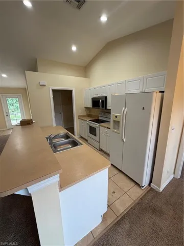 Kitchen featuring vaulted ceilings, white cabinetry, integrated stainless steel microwave, and an island with a double basin sink